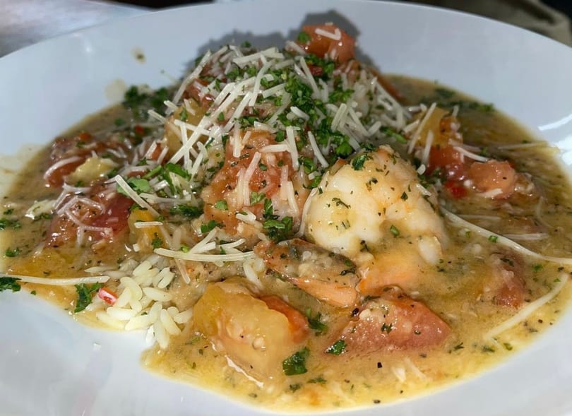 Shrimp and rice dish in a creamy sauce with diced tomatoes, topped with shredded cheese and parsley.