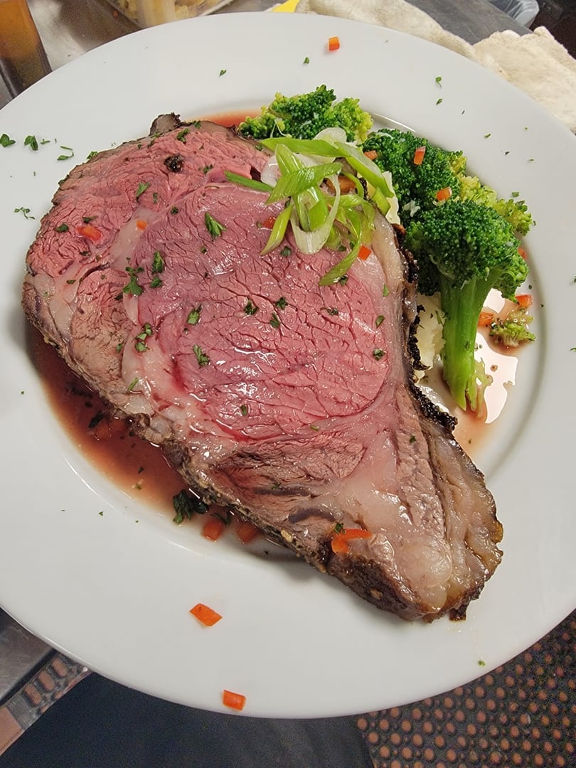 A thick slice of rare prime rib with gravy, garnished with broccoli and scallions.