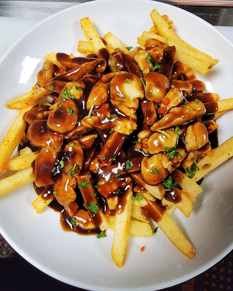 Golden french fries topped with rich brown gravy, mushrooms, and chopped parsley in a white bowl.