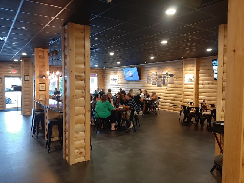 Restaurant interior with wooden walls and columns, people dining at tables, and a bar area.