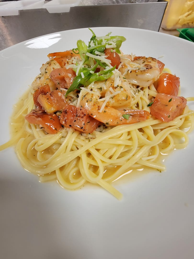 Linguine pasta with shrimp, diced tomatoes, grated cheese, and green onions on a white plate.
